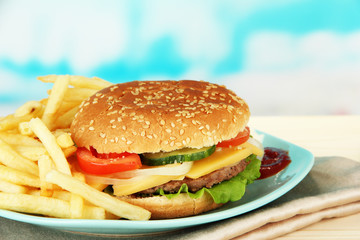 Tasty cheeseburger with fried potatoes, on bright background