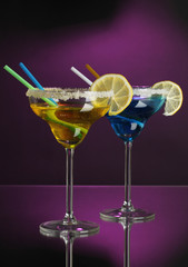 Yellow and blue cocktails in glasses on color background