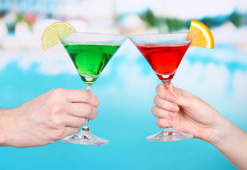 Cocktails in men's and women's hands on pool background