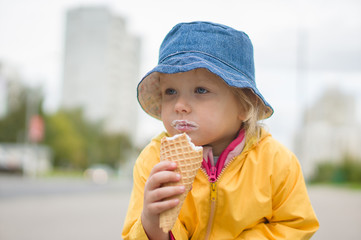 Adorable girl in blue hat eat ice cream on street