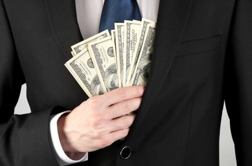 Business man hiding money in pocket on grey background