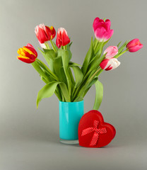 Beautiful tulips in bucket with gifts on grey background