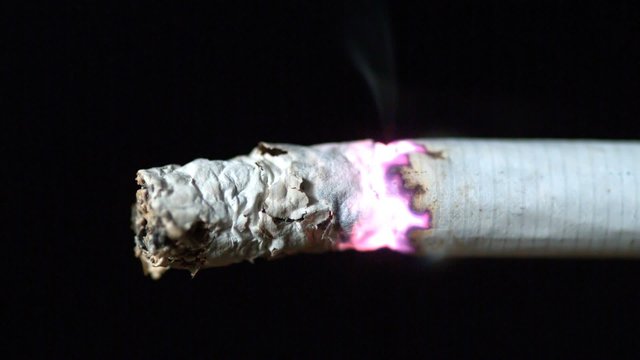 Cigarette burning on black background close up
