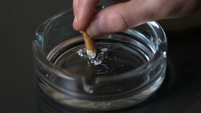 Hand putting out a cigarette in empty ashtray