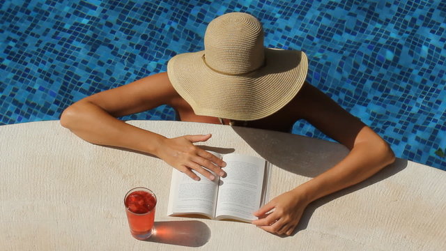 Woman with hat reads by the side of a pool. Tulum, Mexico.