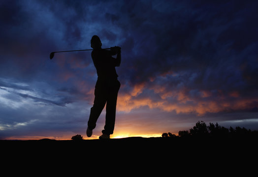 Caucasian golfer swinging golf club at sunset