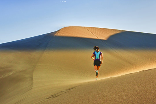 Hispanic woman running on sand dune
