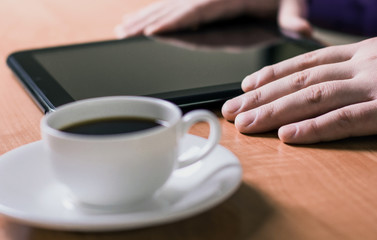 A man holding a cup of coffee and working on a Tablet PC