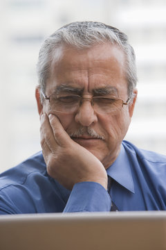 Frowning Hispanic businessman using laptop