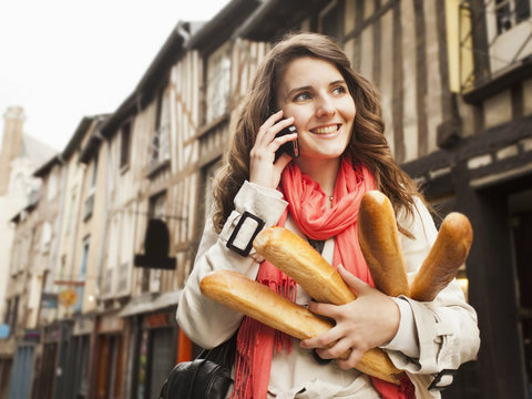 Caucasian woman carrying bread and talking on cell phone