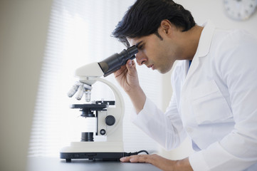 Mixed race scientist peering into microscope