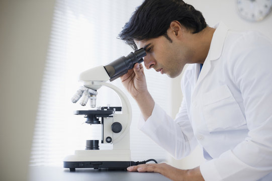 Mixed race scientist peering into microscope