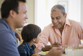 Hispanic grandfather, father and son eating dinner