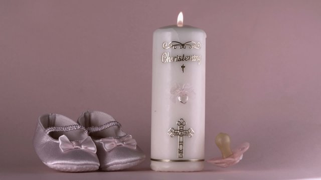 Baby shoes falling beside lit baptism candle and pink pacifier