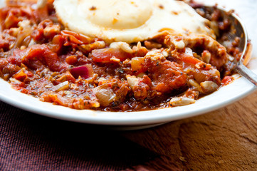 Stewed tomatoes and poached eggs in a bowl with a spoon