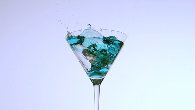 Ice falling into cocktail of blue liquid on white background
