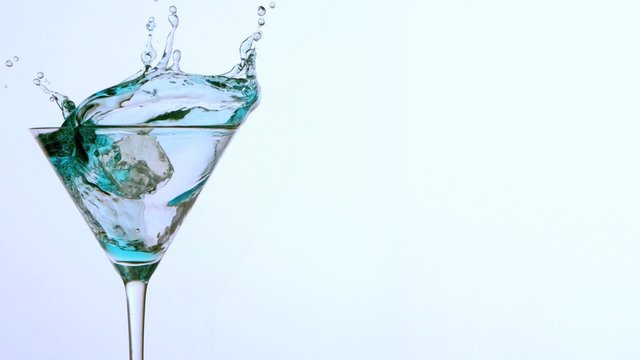 Ice falling into cocktail of blue alcohol on white background