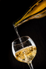pouring white wine into a wineglass on black background