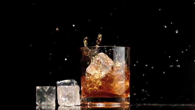 Ice cubes falling into glass of whiskey and ice
