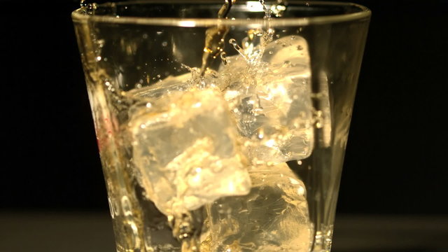 Whiskey pouring into tumbler with ice close up