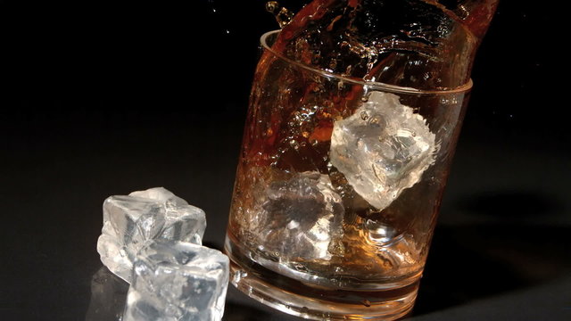 Ice cubes falling into tumbler of whiskey and ice
