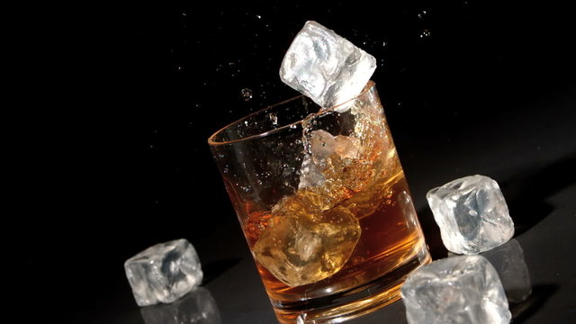 Three ice cubes falling into tumbler of whiskey and ice