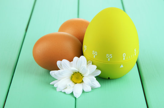 Green egg timer and eggs, on color  wooden background