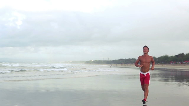 Handsome strong sportsman running along seaside