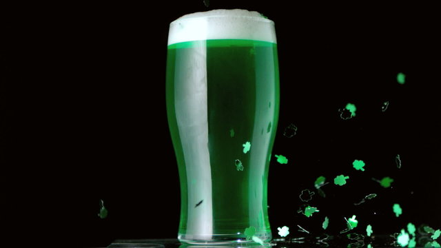 Shamrock confetti falling in front of pint of green beer