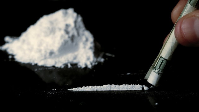 Someone snorting a line of cocaine beside a large pile