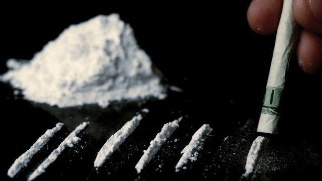 Someone snorting a line of cocaine beside others and a pile