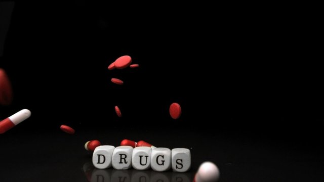 Pills falling and rolling over dice spelling drugs