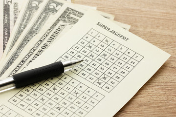 Lottery ticket with pen and money, on wooden background