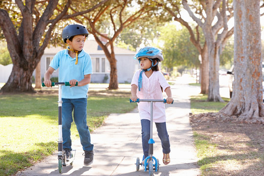 Boy And Girl Wearing Safety Helmets And Riding Scooters