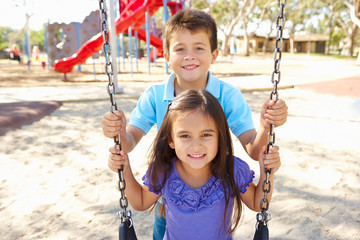 Boy And Girl Playing On Swing In Park