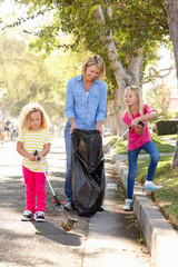 Mother And Daughters Picking Up Litter In Suburban Street
