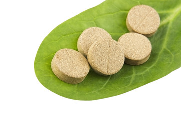 Herbal pills on green leaf isolated on white