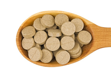 Herbal pills in wooden spoon isolated on white