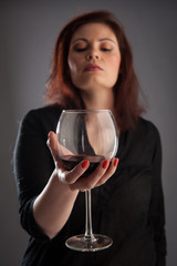 Woman with glass of red wine in her hand on grey background.