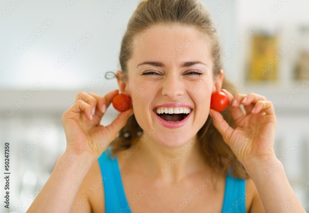 Wall mural Smiling young woman using cherry tomato as earrings