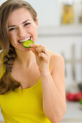 Smiling young woman eating slice of cucumber