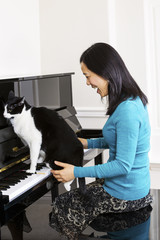 Mature woman and her cat jumping on keyboard of piano