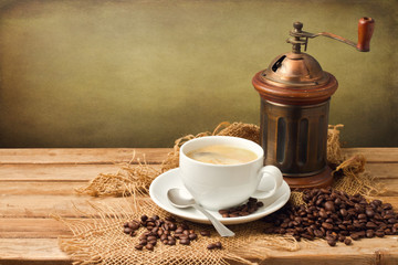 Vintage coffee grinder and coffee cup over wooden background