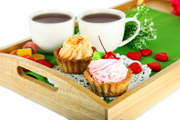 Cups of tea with cakes on wooden tray isolated on white
