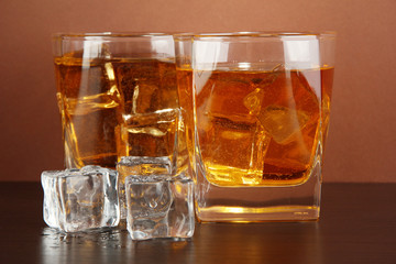 Glasses of whiskey and ice on brown background
