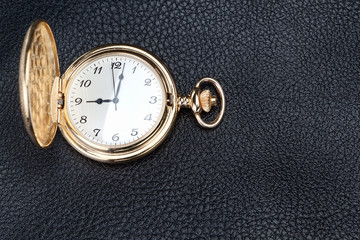 Antique gold pocket watch on a textured black leather. Close-up.