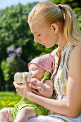 Young mother feeds her baby from bottle in spring park