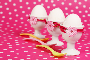 Drei Eierbecher mit Eiern vor Pünktchen Hintergrund