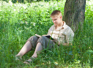 Naklejka na ściany i meble The young man reads the book on the river bank