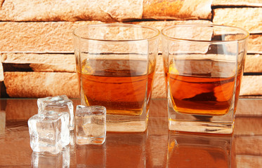 Glasses of whiskey and ice on brick wall background